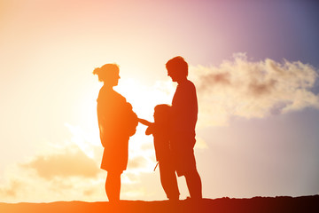 happy pregnant mother and father with son at sunset