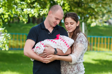 Happy couple holding their newborn daughter in her arms. Outdoors