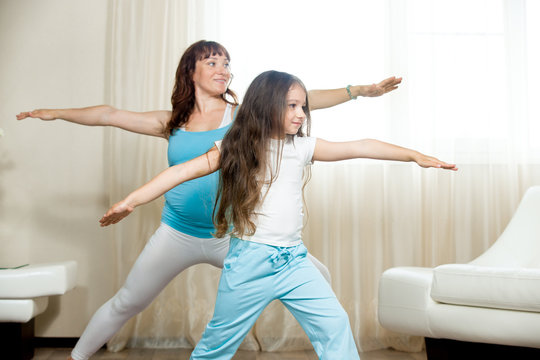 Family healthy lifestyle concept. Pregnancy Yoga and Fitness. Young happy pregnant yoga mom working out with kid girl in living room interior. Pregnant mother and child doing sport training at home