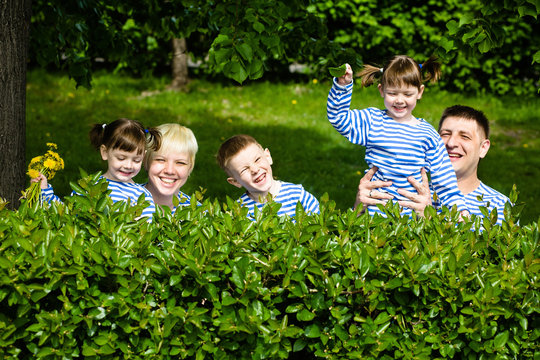 Happy family: mother, father, son and daughters-twins in striped T-shirts having fun in the park on a sunny summer day