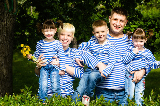 Happy family: mother, father, son and daughters-twins in striped T-shirts having fun in the park on a sunny summer day
