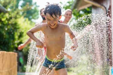 Boy cooling down with garden hose, family in the background
