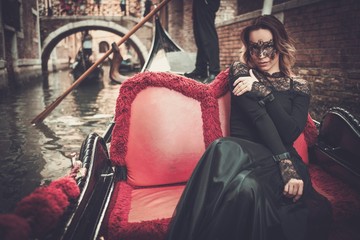 Fototapeta na wymiar Beautiful woman in black dress with carnaval mask riding on gondola. 