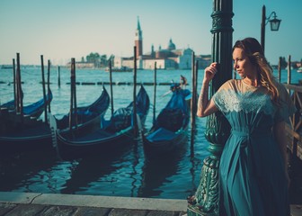 Fototapeta na wymiar Beautiful well-dressed woman standing near San Marco square with gondolas and Santa Lucia island on the background. 