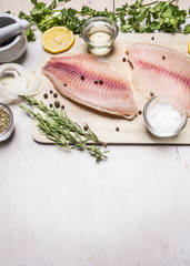 raw fillet of tilapia with spices and herbs, lemon and pepper on a cutting board on a white background rustic village