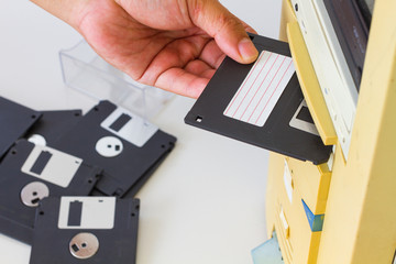 Hand inserting a 3.5-inch floppy disk into a floppy drive slot on a desktop computer. Selective...