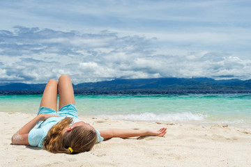 young beautifull girl lies on the white sand of tropical beach under cloudy sky