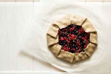 Homemade galette pie with red and black currants, blueberries and raspberries on wooden background. Top view