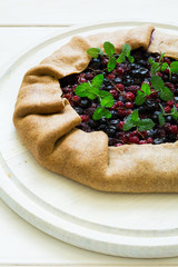 Homemade galette pie with red and black currants, blueberries and raspberries on wooden background. Top view