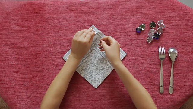 Female hands artistically fold napkin and put fork and knife inside it. Table decoration.