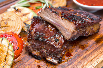 Grilled ribs on a wooden board with vegetables