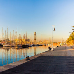 Mooring for yachts and boats in the port of Barcelona at sunrise. The ships moored in the harbor city at sunrise with the reflection of the masts in the water. Spain.