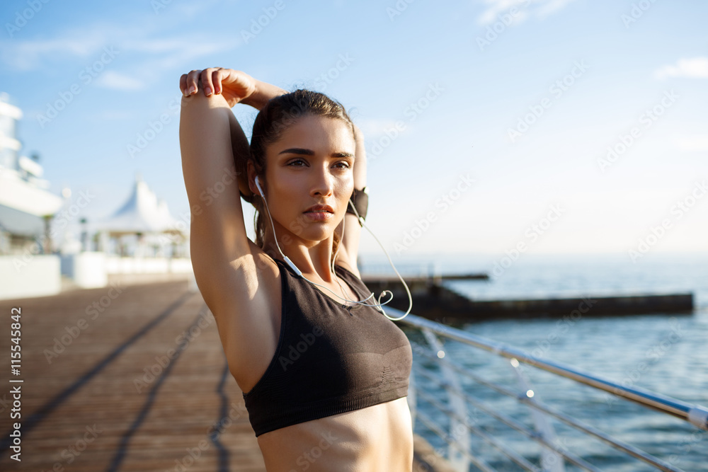 Wall mural Picture of young beautiful fitness girl makes sport exercises with sea coast on background