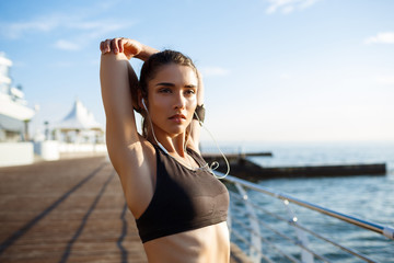 Picture of young beautiful fitness girl makes sport exercises with sea coast on background