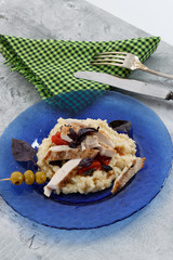 Traditional italian risotto with chicken, tomato, basil and parmesan on blue plate with knife and fork and glass of wine