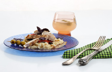 Traditional italian risotto with chicken, tomato, basil and parmesan on blue plate with knife and fork and glass of wine