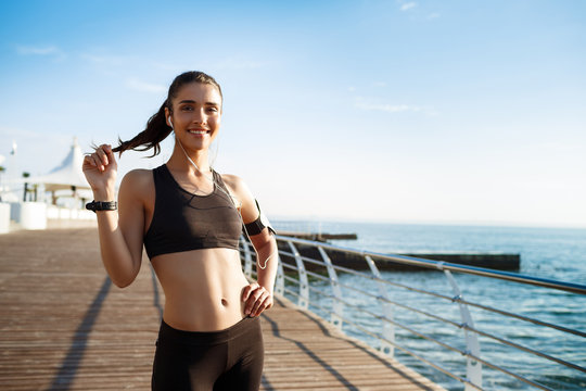Picture of young smiling fitness girl ready for sport exercises with sea coast on background