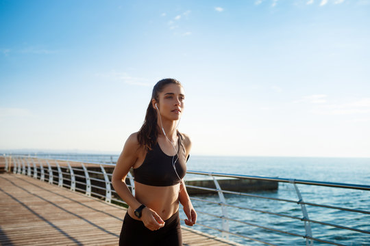 Picture of young attractive fitness girl running with sea coast on background