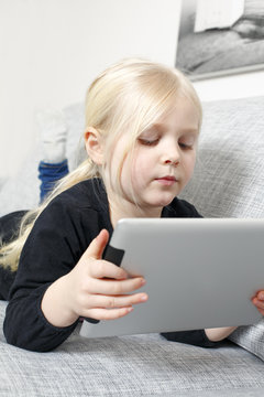 Sweden, Girl (4-5) using digital tablet while lying on sofa
