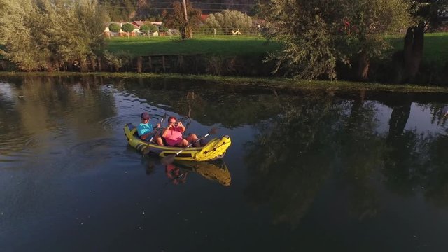 AERIAL: Couple kayaking on river, woman takes picture of pretty nature