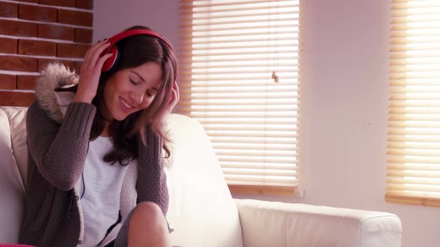 Smiling woman listening to music with headphones on sofa 