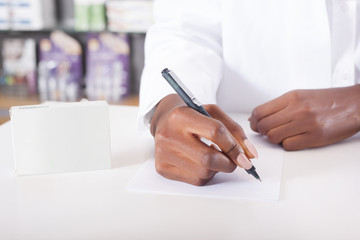 Black pharmacist or doctor writing with green tablet package with copy space