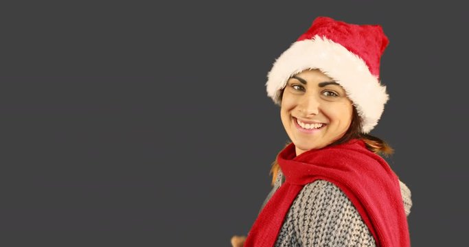 Girl in santa hat and warm clothing blowing over hands on grey background