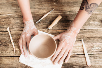 Pottery molding on wooden table top view. Artisan hands with clay bowl and special tools flat lay , creativity in arts