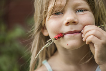 Sweden, Portrait of girl (4-5) with wild strawberries on spikelet in mouth