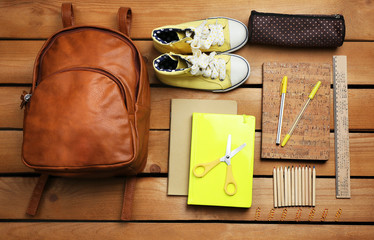 School set with backpack, shoes and supplies on wooden background