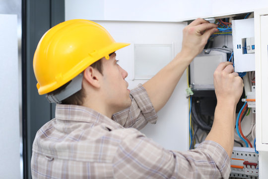 Young electrician checking voltage in fuse board