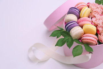 Tasty macaroons and roses in box on light background