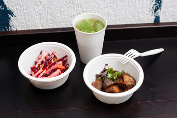 Vegetarian fastfood - plastic plates with salad and stew eggplants and a glass of lemonade