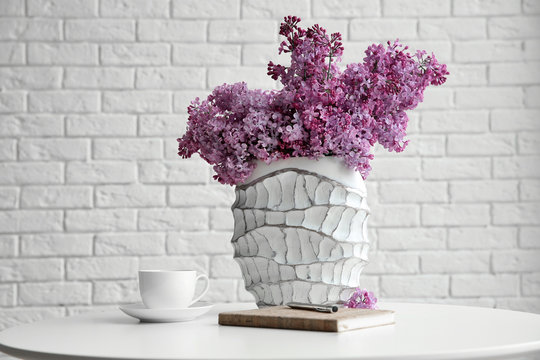 Purple lilac flowers in a vase on white brick wall background