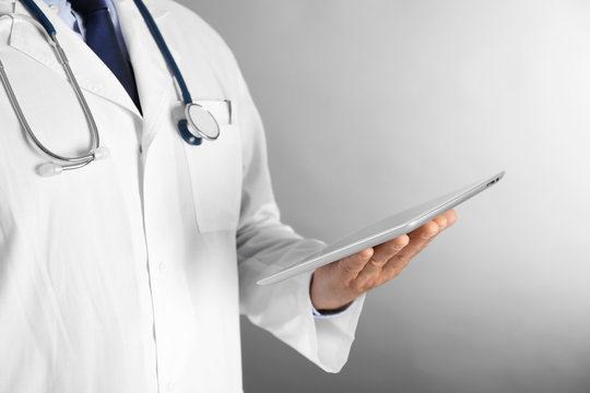 Professional doctor with tablet on grey background
