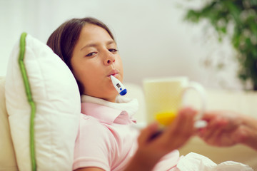 Cold girl lying on the couch with a thermometer in her mouth