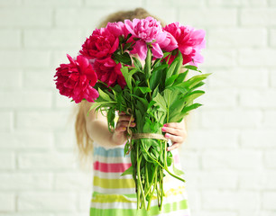 Girl holding fresh peonies bouquet on brick wall background