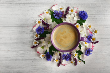 Obraz na płótnie Canvas Cup of coffee with fresh flowers lying around on wooden background