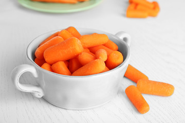Small baby carrots in bowl on light wooden background