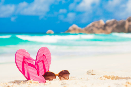 Pink flip flops and sunglasses on a tropical sea resort background