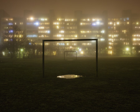 Sweden, Skane, Malmo, Rosengard, Illuminated residential buildings with soccer field in foreground in fog