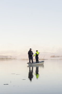 Sweden, Vastmanland, Bergslagen, Torrvarpen, Young men fishing in lake at sunset