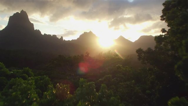 AERIAL: Flying above tropical jungle with sunset behind rocky mountains