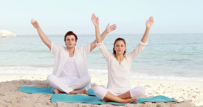 Peaceful couple meditating at the beach