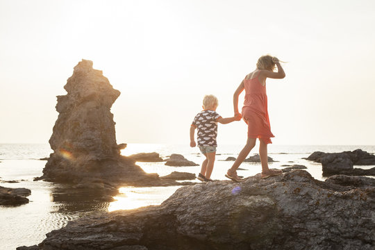 Sweden, Gotland, Faro, Gamle hamn, Girl (8-9) walking with brother (2-3) on coastal rocks 