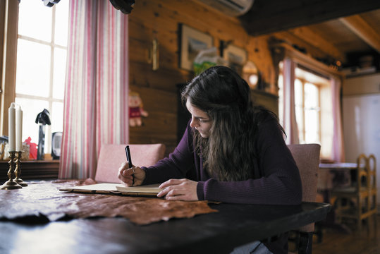 Sweden, Young woman sitting at table and writing in dairy