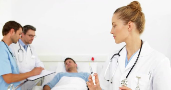 Doctors speaking with sick patient in bed while nurse prepares needle