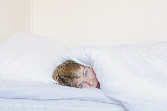 Portrait of young man wrapped in blanket lying on bed