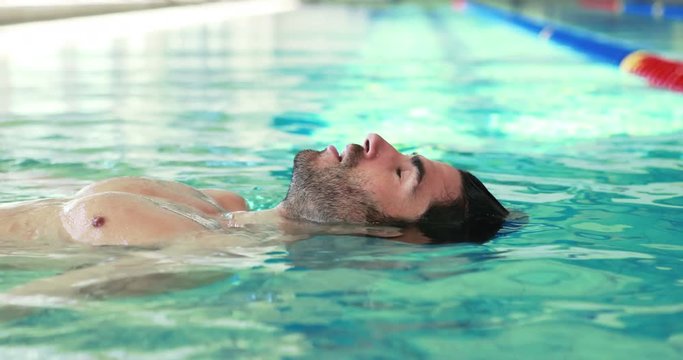 Muscular man floating with closed eyes in swimming pool