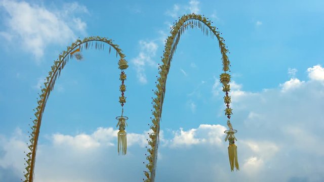 Pair of traditional, Balinese Penjors; offerings to ancestral spirits suspended on the ends of long bamboo poles, standing against the sky. Video UltraHD